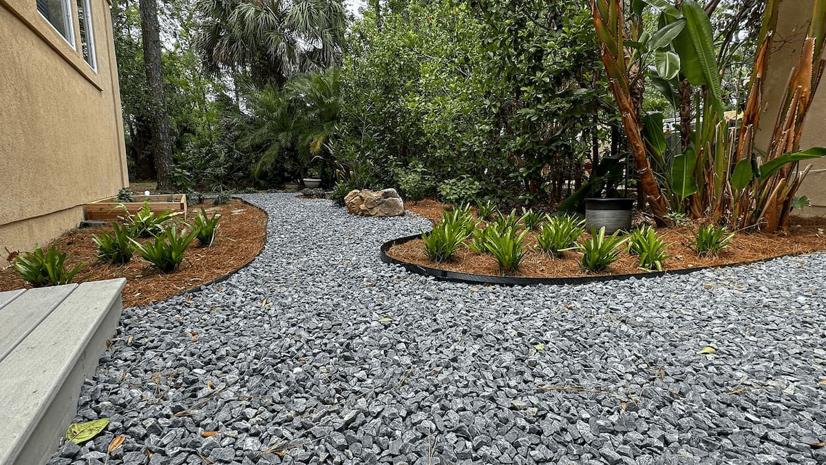 Backyard with stone path, lush greenery, and landscaped beds by Rockaway Sustainable Landscaping