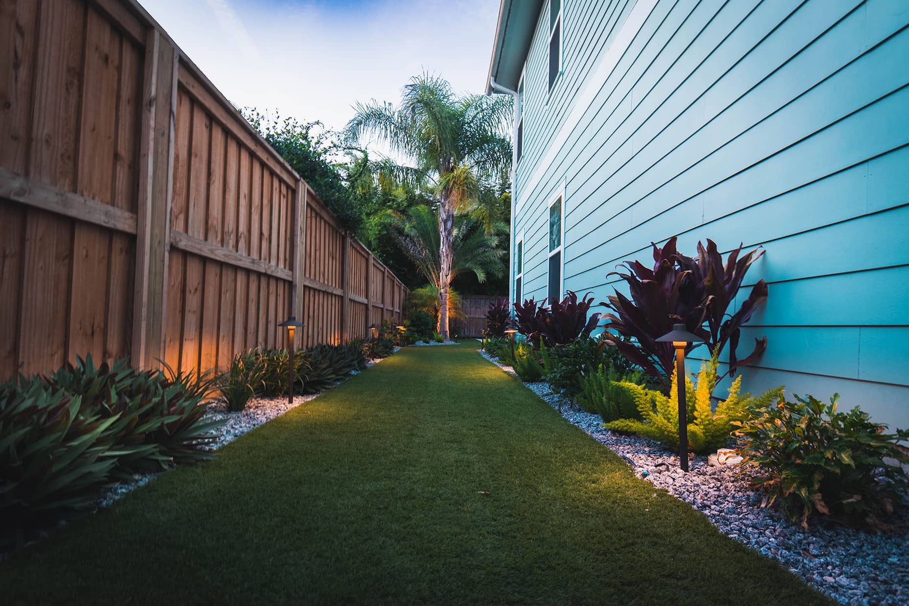 Backyard walkway with lawn, plants, and warm landscape lighting by Rockaway Sustainable Landscaping